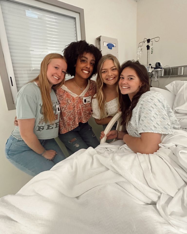 A group of four women one on a hospital bed gathered closely and smiling inside a medical room