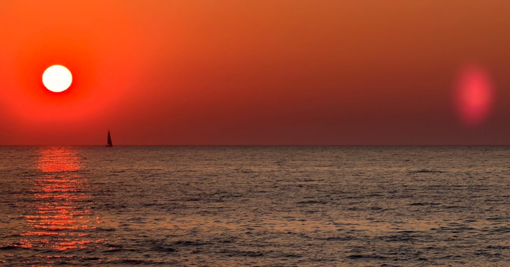 Vibrant red sunset over Lake Michigan with a silhouette of a sailboat on the horizon.