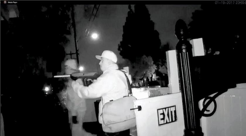 Two men, one holding a long gun to his shoulder, are pictured at night on a city street.
