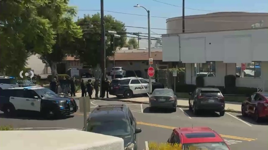 Police officers surround a commercial building as a shirtless man holding a machete is seen during a standoff that ended in an officer-involved shooting