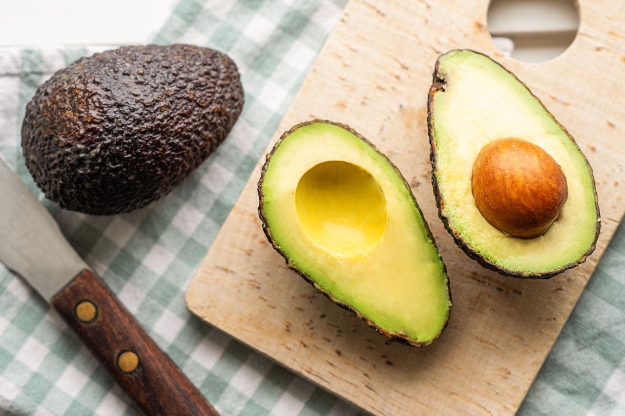 halved avocado on a cutting board, and on the counter, a whole avocado and a knife