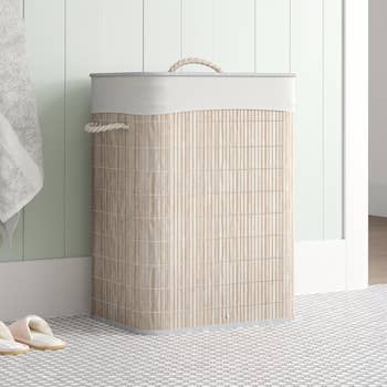 Woven laundry hamper with rope handles in a bathroom setting next to a towel and slippers