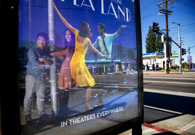 A couple is reflected in a bus stop movie poster for