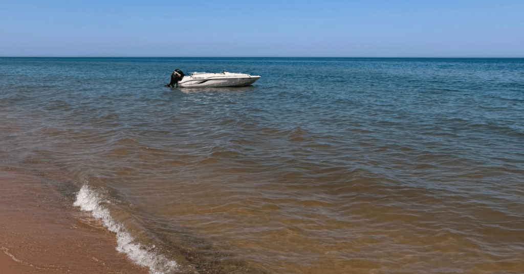 Motorboat anchored in Lake Michigan near the sandy shore at Nordhouse Dunes Wilderness.