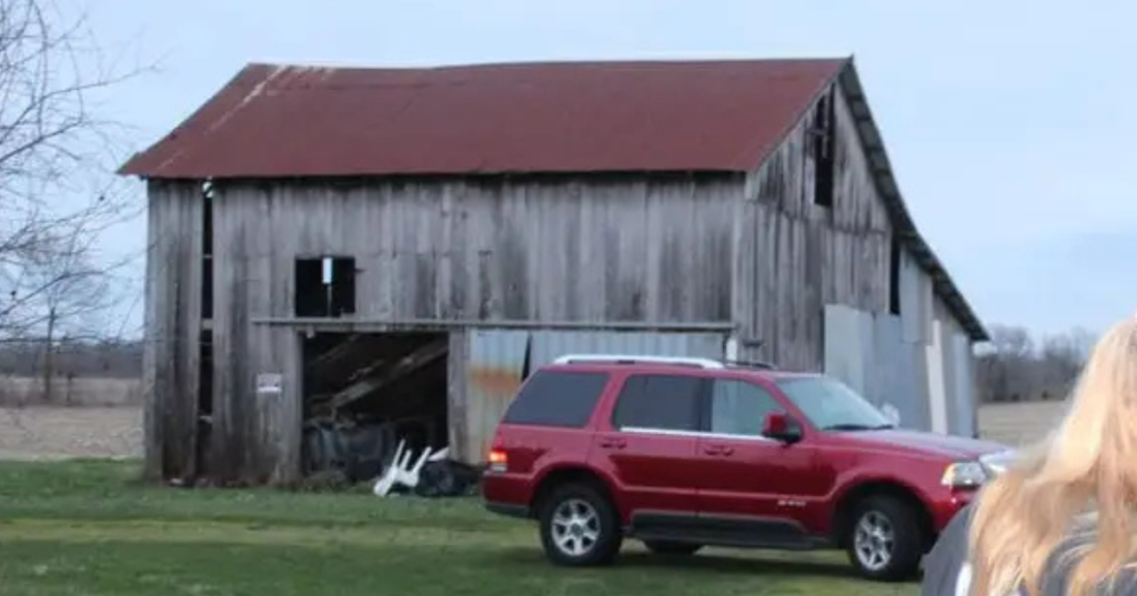 Red SUV parked outside an old rustic wooden barn at Revenant Acres Farm attraction in Indiana.