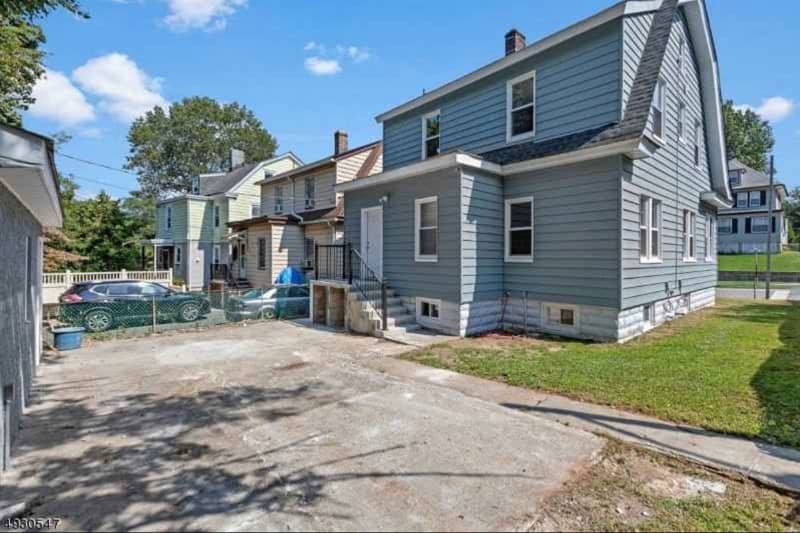Empty concrete area between garage and blue house with side lawn.