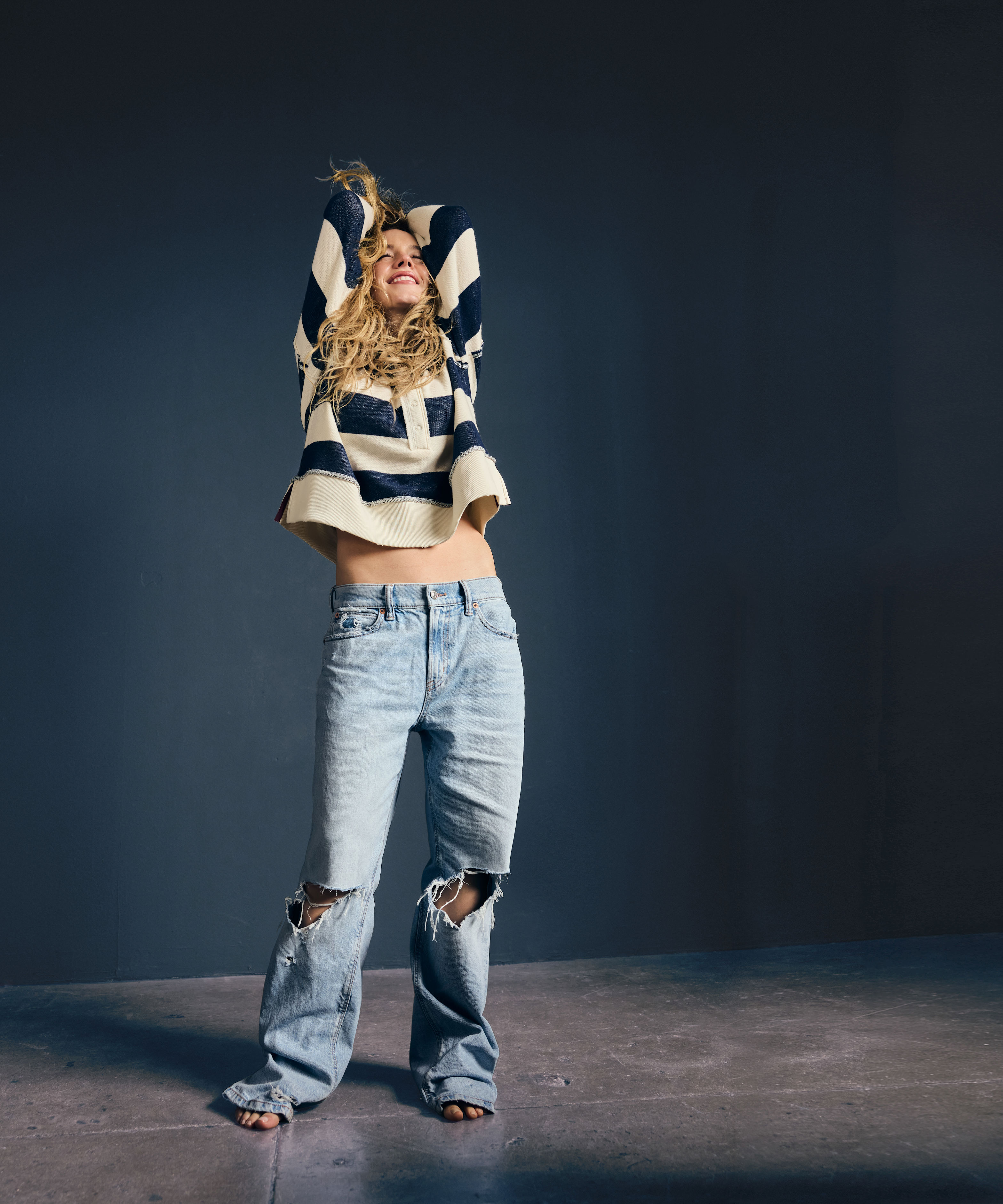 Sydney Sweeney in a blue and white striped shirt and ripped jeans.
