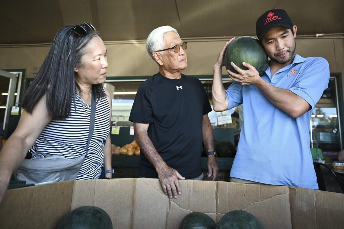 Derek Ikeda, right, shows Debbie Ford, left, and Ronald Akune of Sacramento how he selects a ripe watermelon at Ikeda’s in Auburn on Sunday, July 19, 2026.
