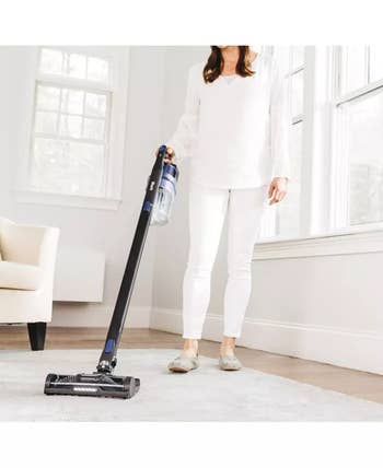 Person using a cordless vacuum on a carpeted floor in a bright, minimalist room