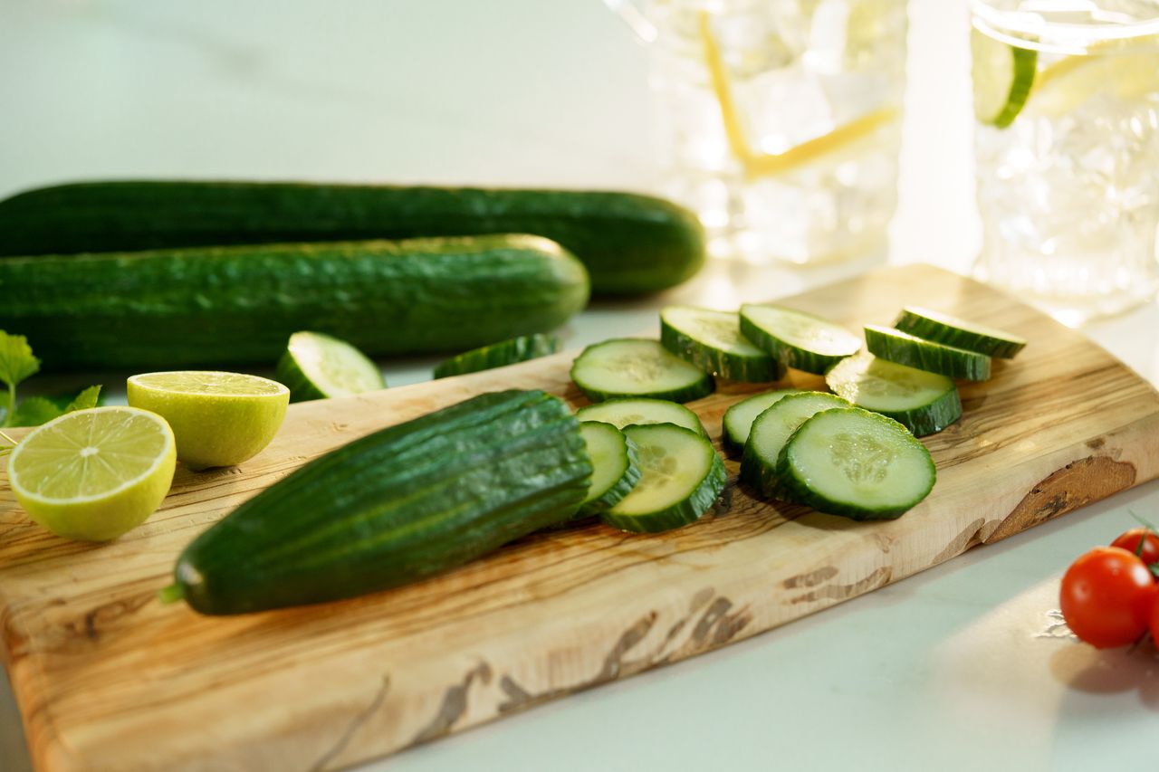High angle of cut ripe cucumber and halved lime on wooden chopping board