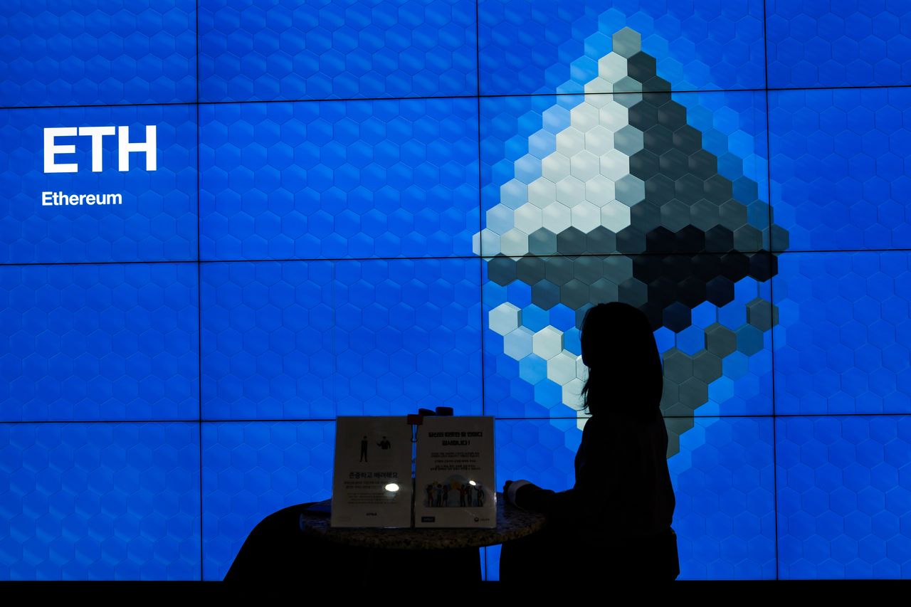 A woman sitting in front of a digital screen showing Ethereum's brand logo and symbol.