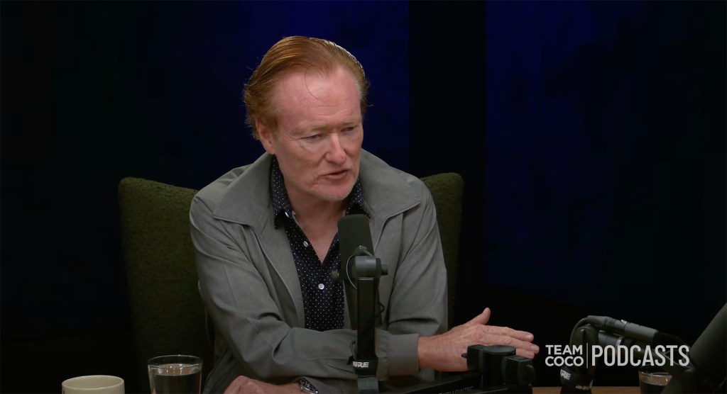 Conan O'Brien speaking into a podcast microphone.