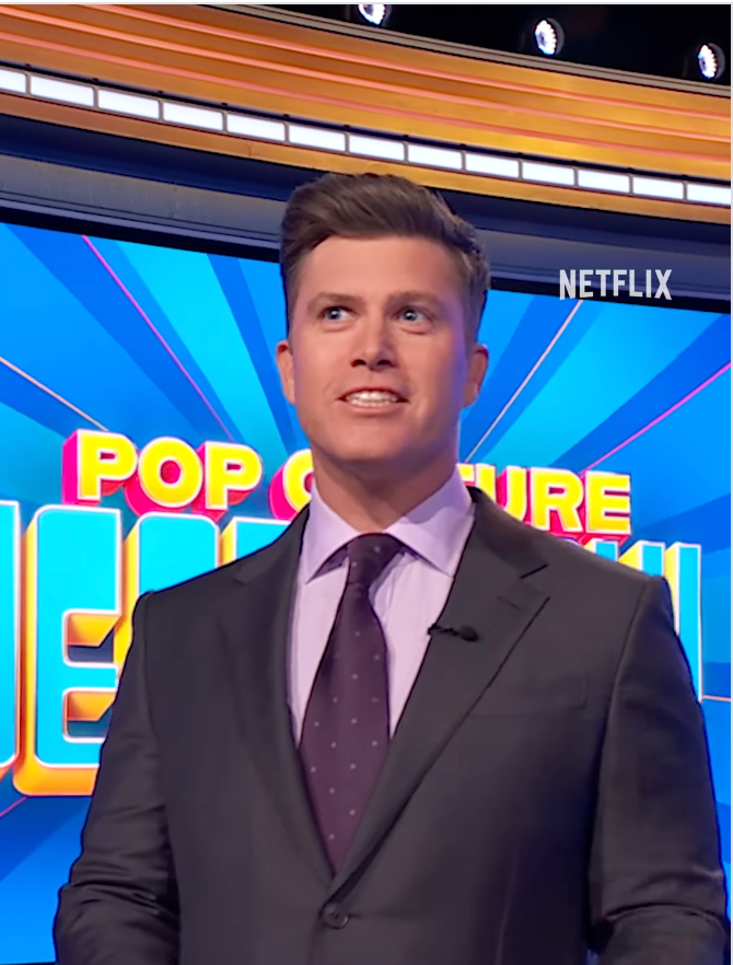 Person in a suit on a game show set with "Pop Culture" visible in the background