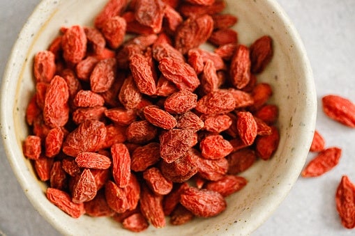 A bowl filled with dried goji berries on a light surface