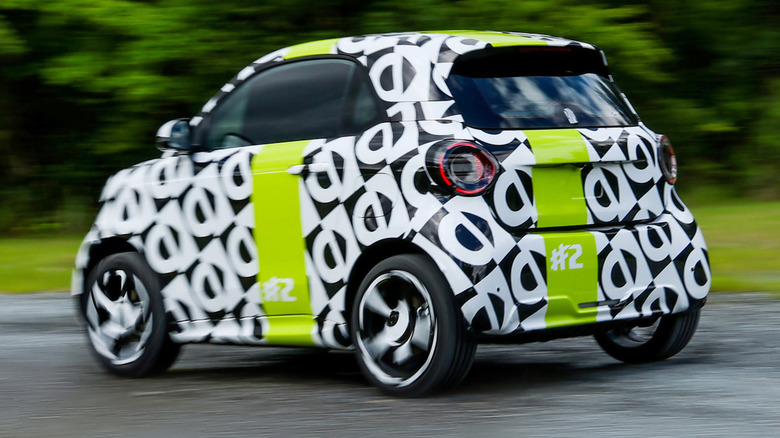 A rear three-quarters shot of the black-and-white camouflaged #2 driving past hedges