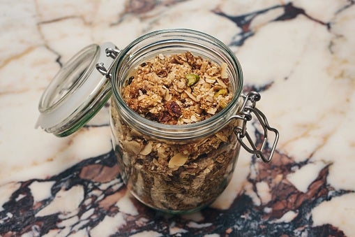 A jar filled with mixed granola, including nuts and seeds, on a marble surface