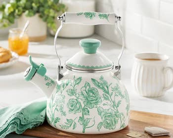 Floral-patterned 2-quart (1.9L) teapot on a kitchen counter, next to tea items and a green cloth