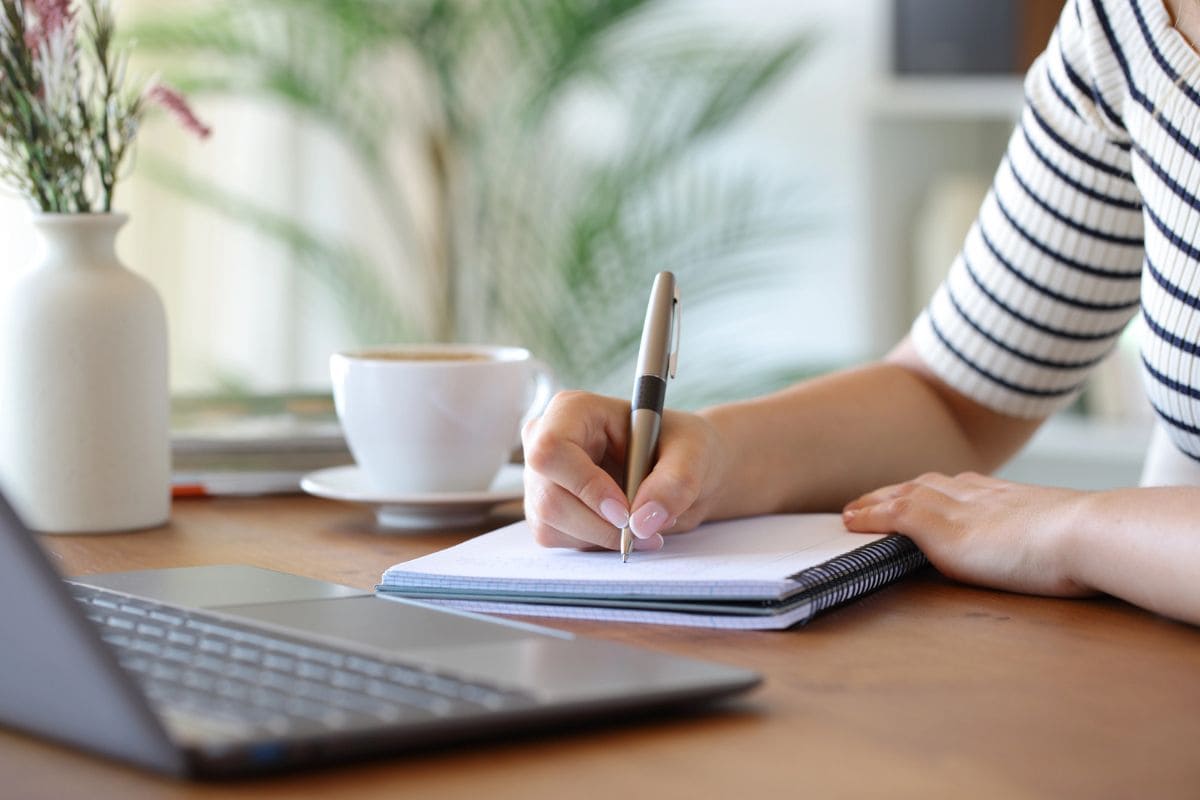A woman sitting at her kitchen table writing in a notebook.