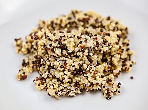 A close-up of a pile of cooked quinoa with a mix of white, red, and black grains on a white surface