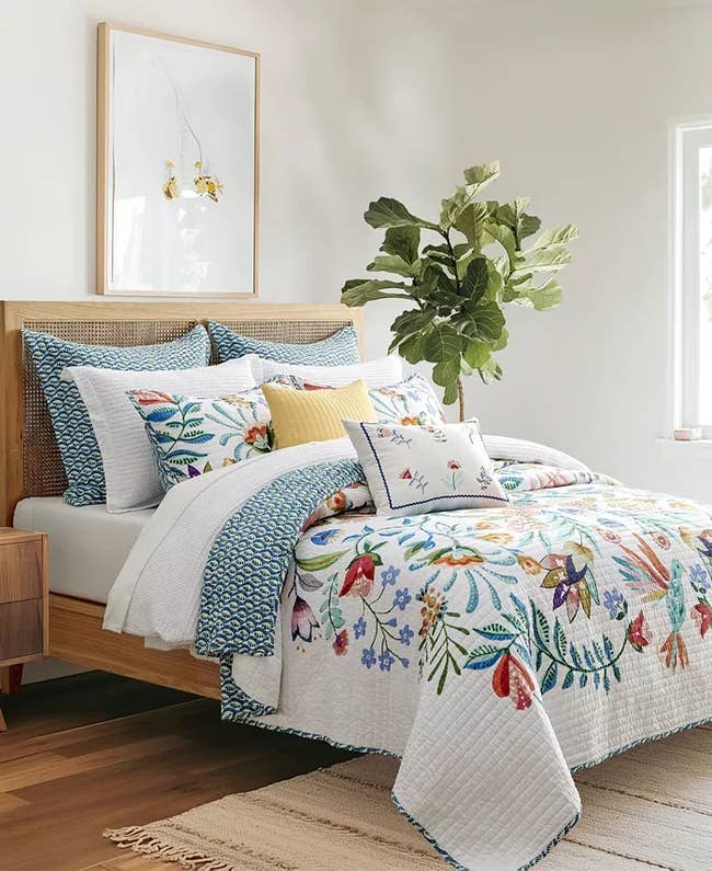 Stylish bedroom featuring a bed with floral-patterned bedding, multiple pillows, and a large plant in the corner, creating a cozy and inviting look