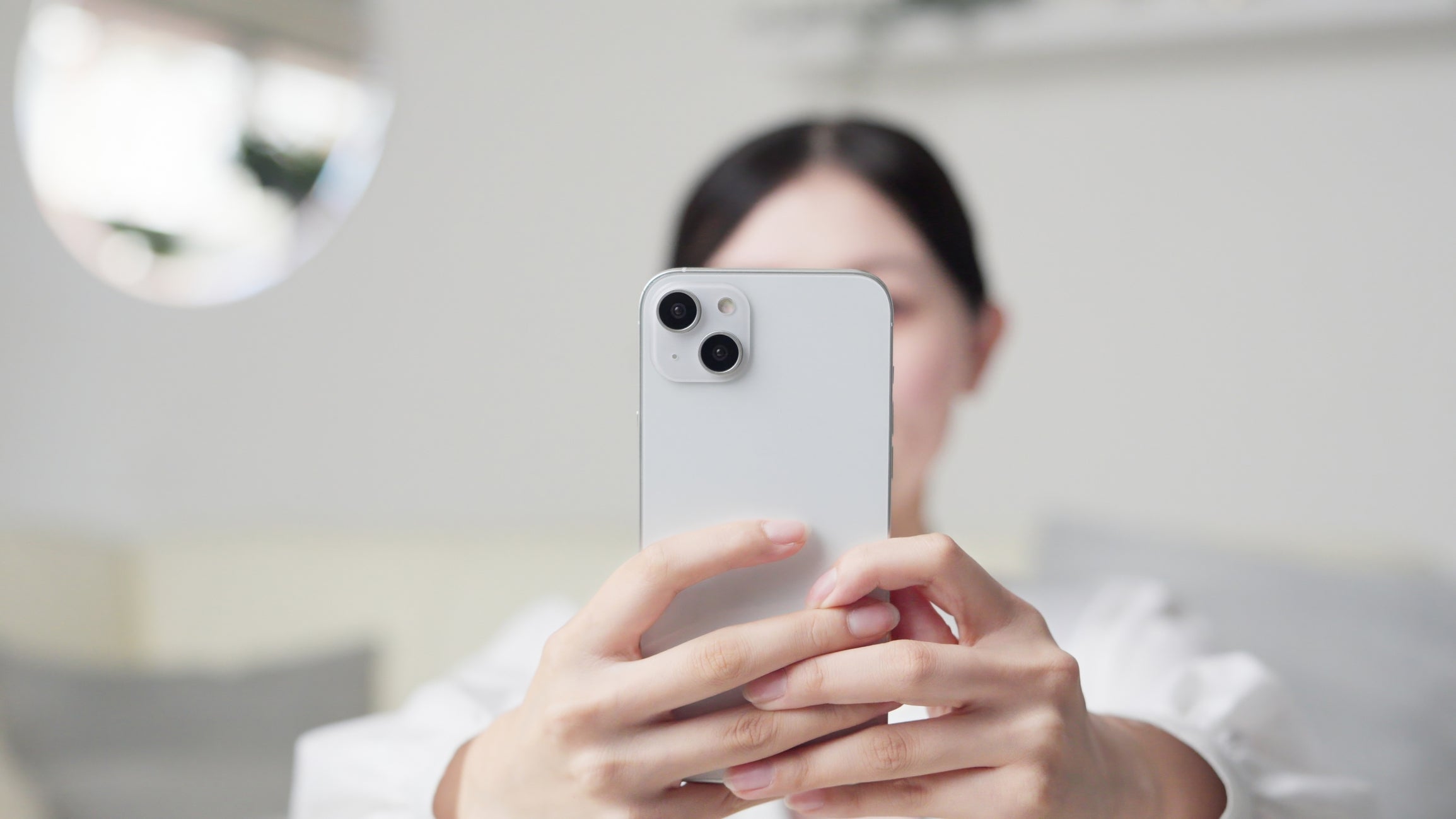 Person holding a smartphone for a selfie, face blurred in the background, indoors