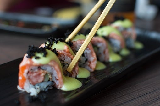 Sushi rolls topped with avocado sauce and black fish roe, neatly arranged on a black plate