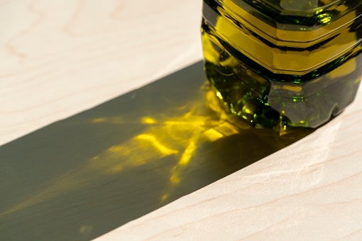 Glass bottle casting a light-reflecting shadow on a surface, highlighting its patterned base