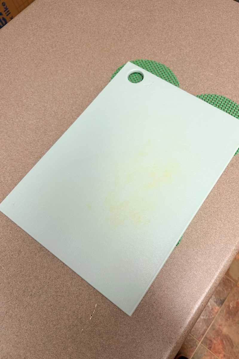 Light green cutting board with a small hole in the corner, resting on a brown countertop.
