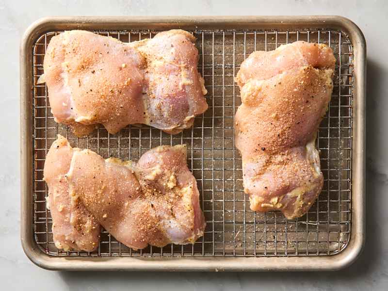 Raw chicken thighs seasoned with spices on a wire rack in a baking tray.