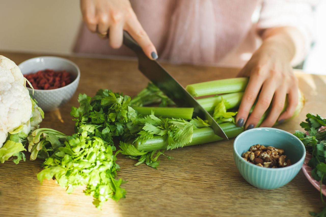 A woman's hands cutting celery on a wooden table