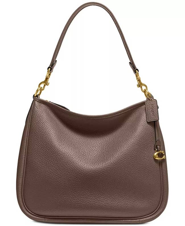 A brown leather handbag with a single strap, featuring gold hardware, and a small charm detail on the side. Ideal for shopping and style