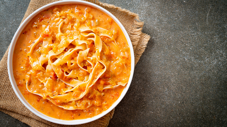 A bowl of fettuccini in pink sauce on a burlap placemat