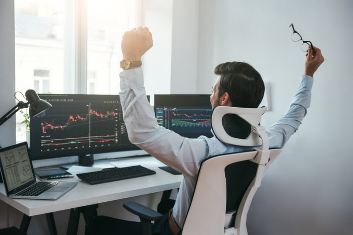 Investor celebrating at a computer screen displaying stock charts.