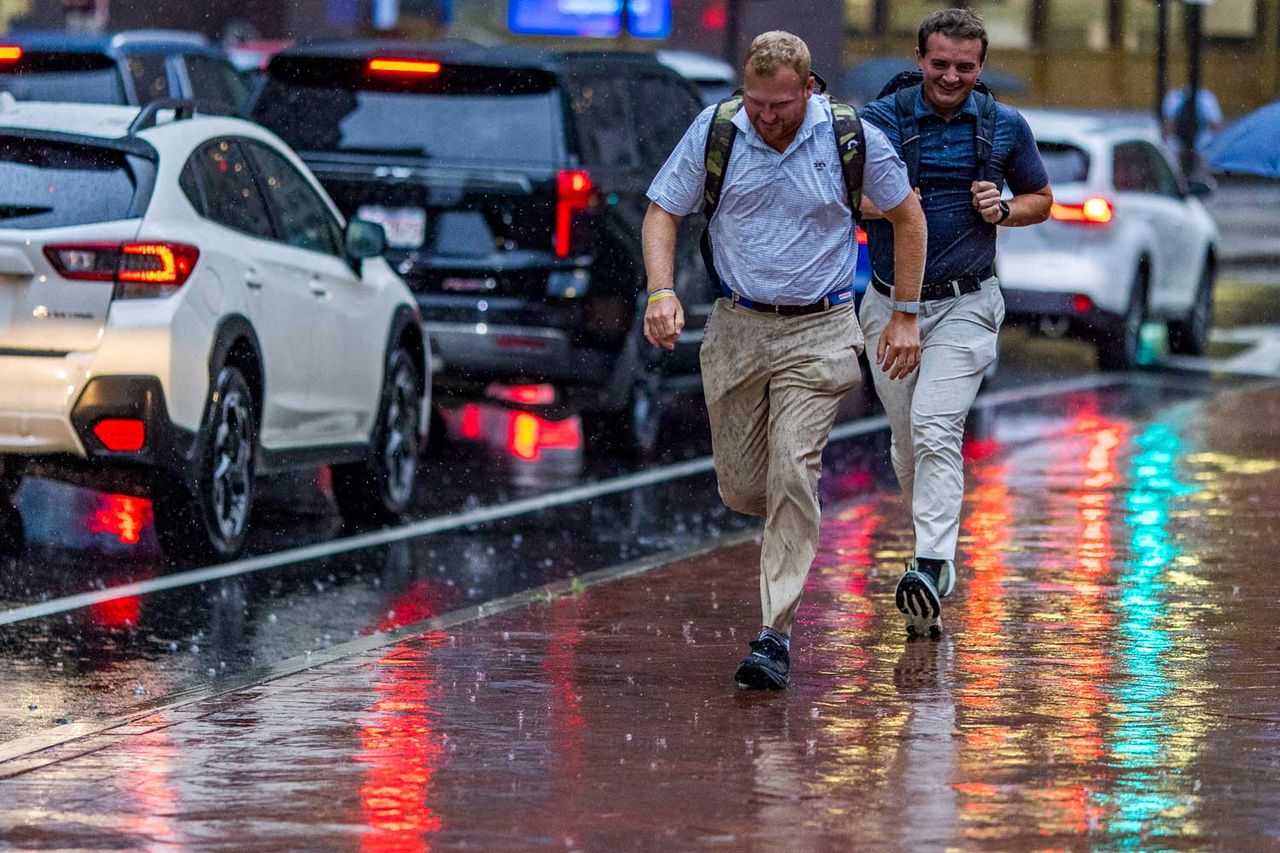 People run in the rain after getting off of work on July 21, 2026