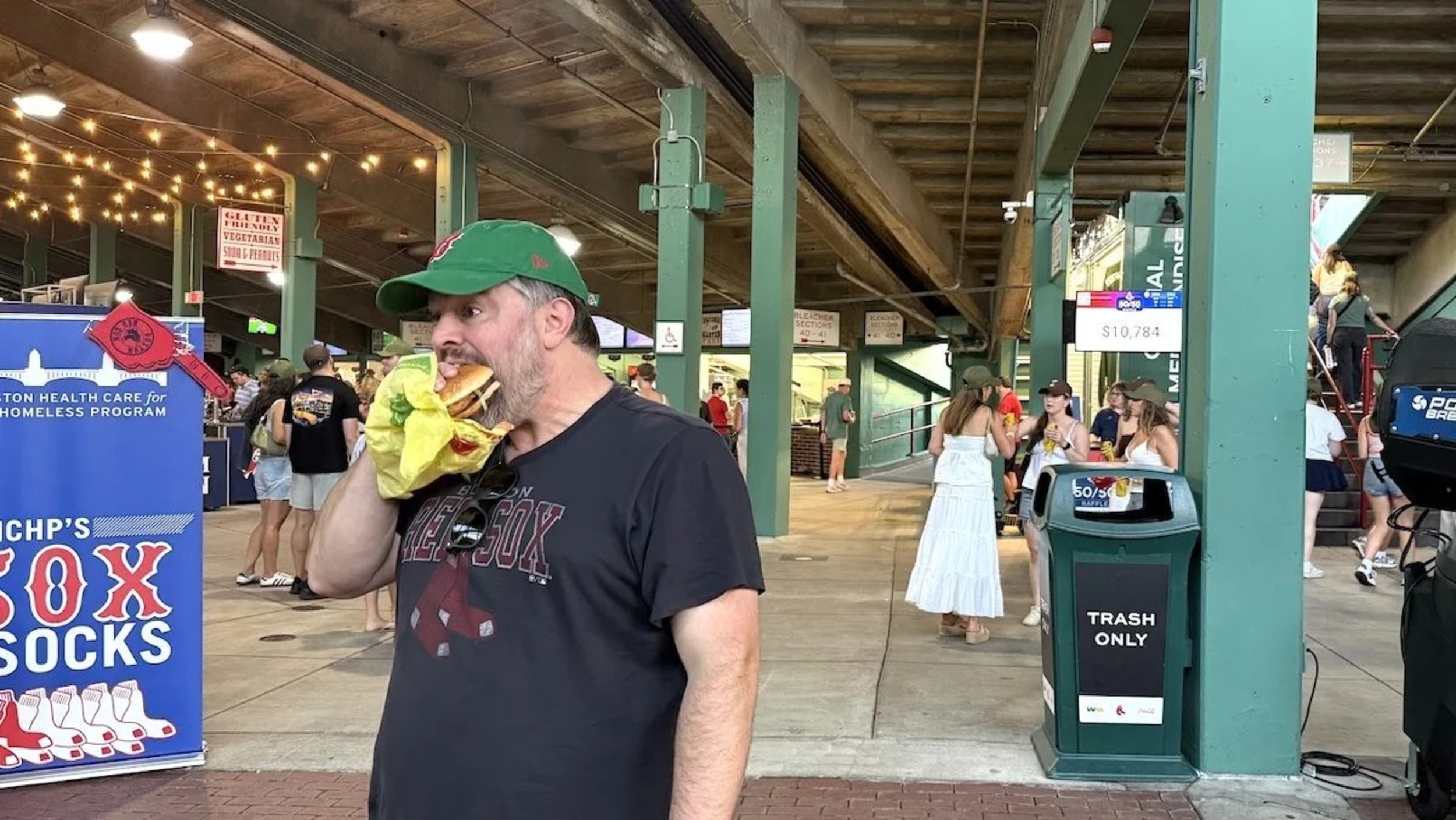 A bearded man in a green hat eating a McChicken in Fenway Park's concourse