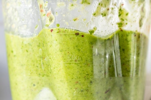 Close-up view of a green smoothie being blended, showing its creamy texture and specks from blended ingredients