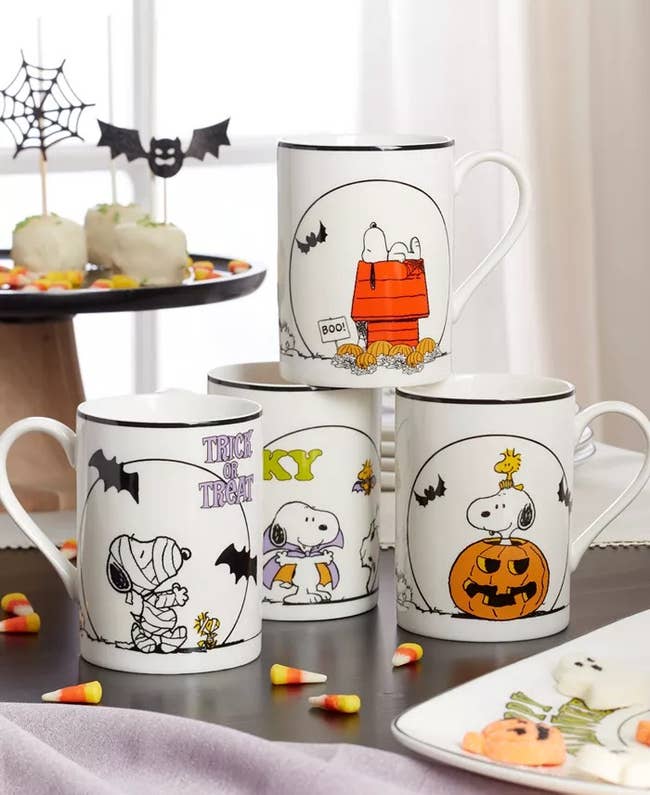 Halloween-themed mugs featuring Snoopy designs are showcased with festive treats and decorations