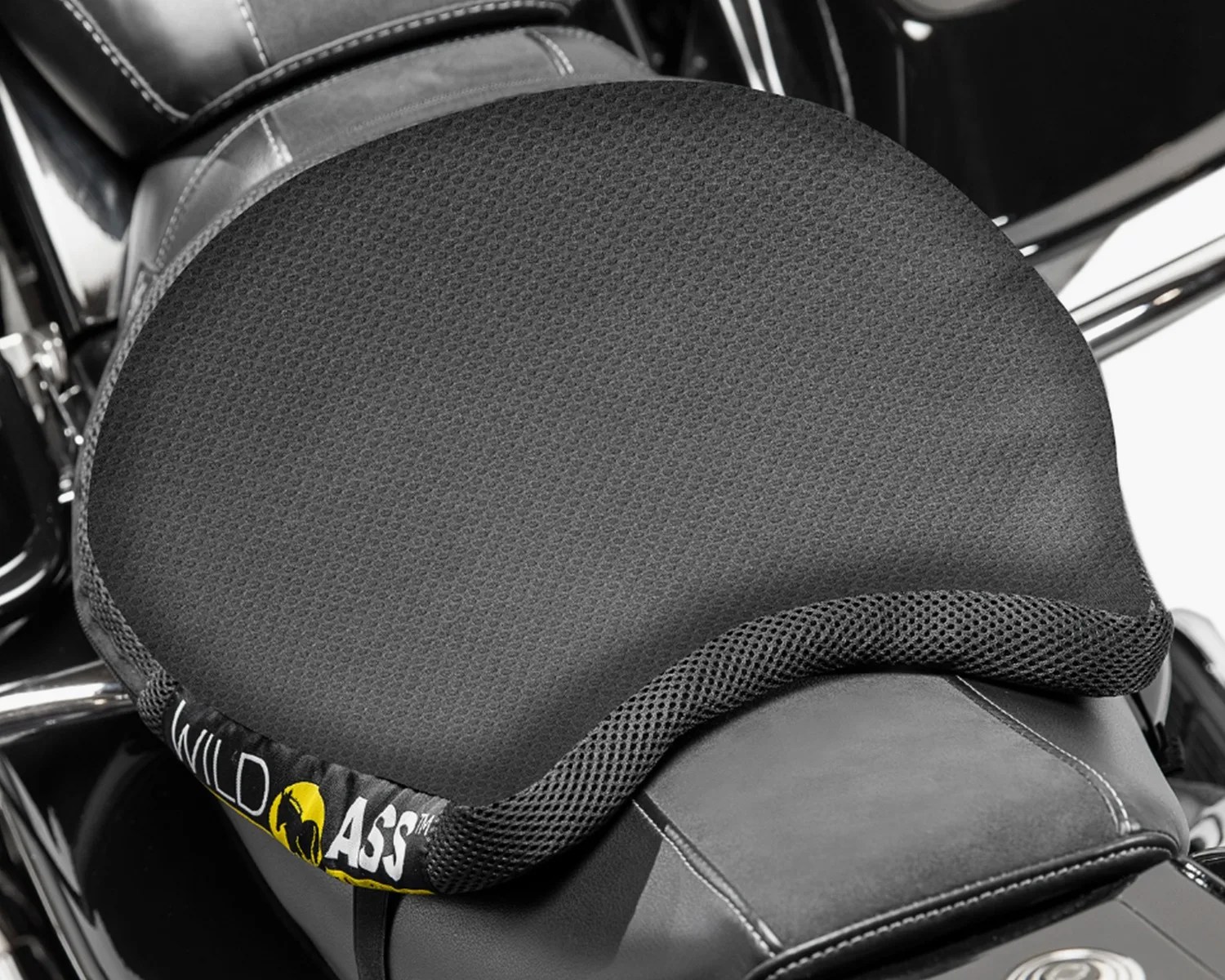 Black textured motorcycle seat cushion with mesh edge and "Wild Ass" logo on a leather seat.