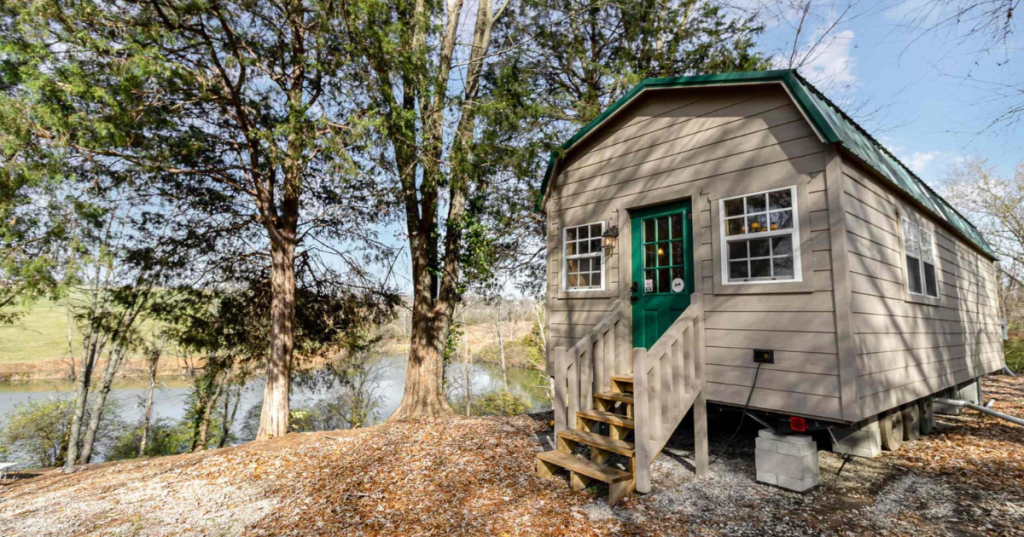 The exterior of a tiny home Airbnb in Dry Ridge, Kentucky, next to tall trees. Bolz Lake is visible to the side of the home.