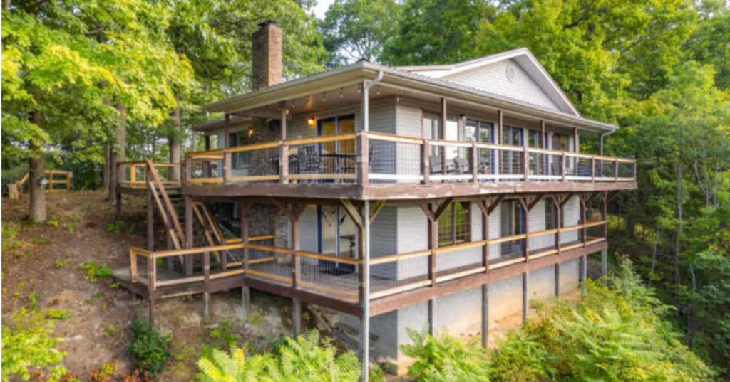 The exterior of a two-story Airbnb in Kentucky built on a hillside and surrounded by lush green trees.
