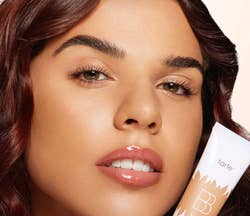 Person holding a tube of Tarte BB cream close to their face, showcasing smooth and glowing skin. Suitable for beauty shopping content