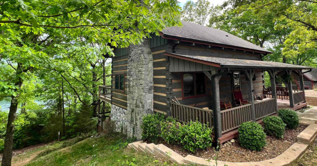 The exterior of a small log cabin on a summer day in Kentucky, surrounded by green grass and tall trees.