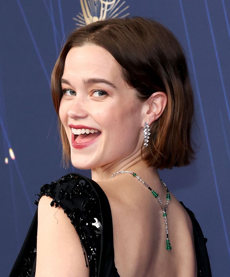 A person smiling over their shoulder at an event wearing pendant earrings and a necklace