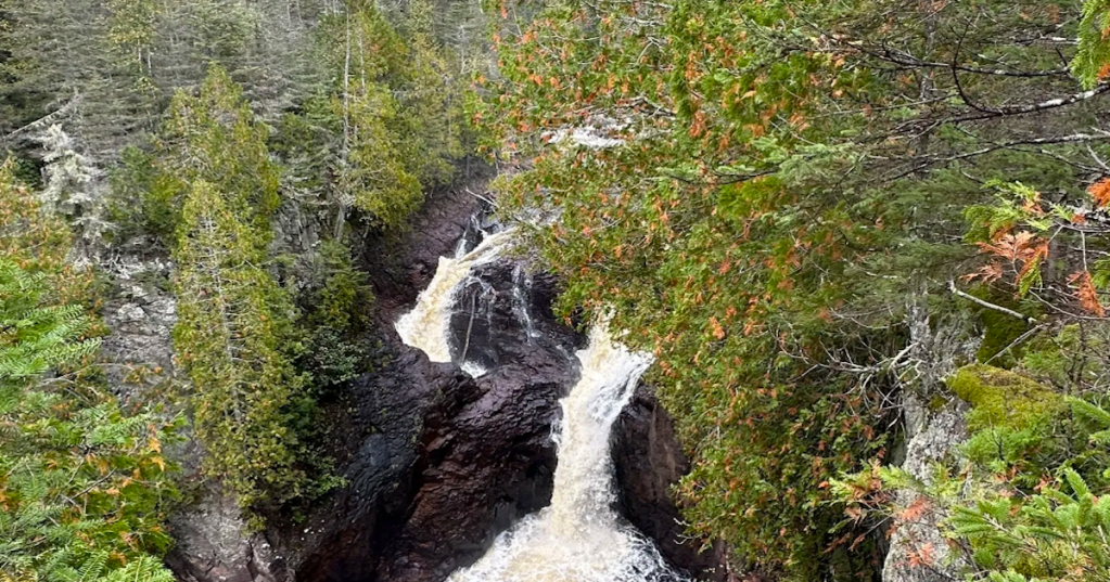 Overlook view of the split waterfall cascading into a rocky canyon with autumn trees in Minnesota.