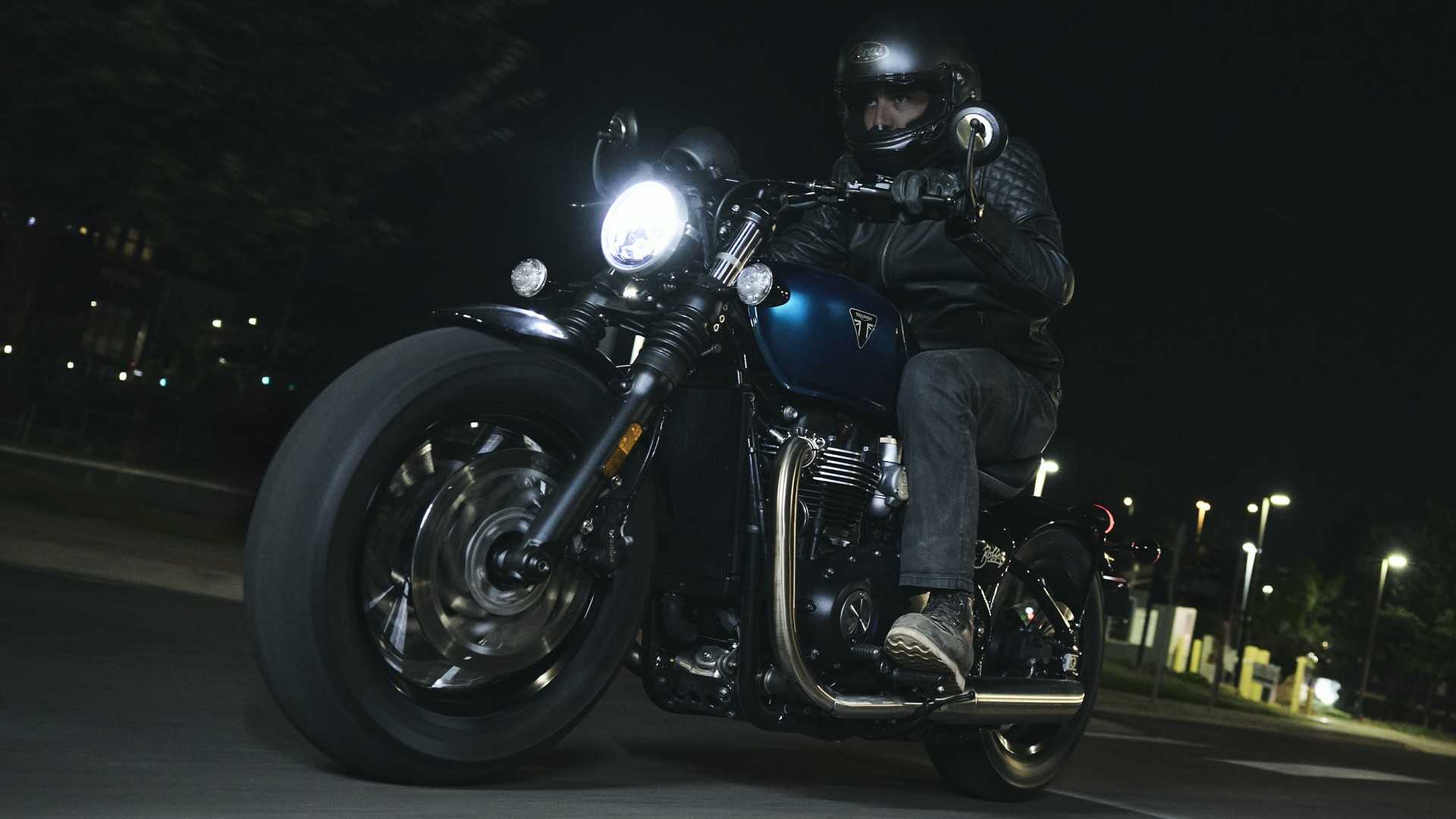 2026 Triumph Bonneville Bobber accelerating hard at night cinematic front third quarter view