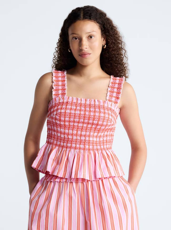 Person wearing a sleeveless, ruffled, smocked top with vertical striped pants
