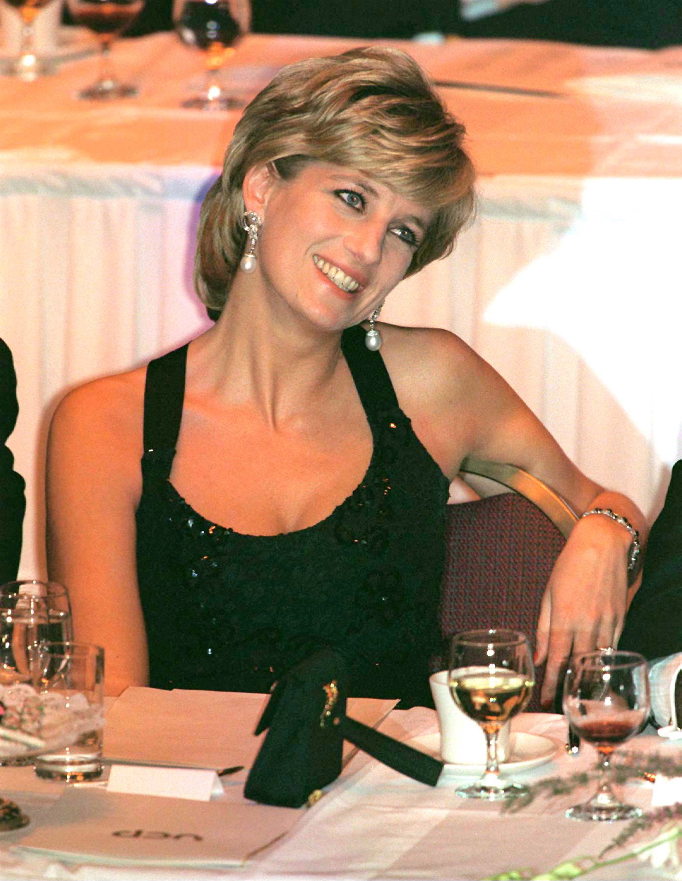 Princess Diana wearing a black dress sitting at a dinner table