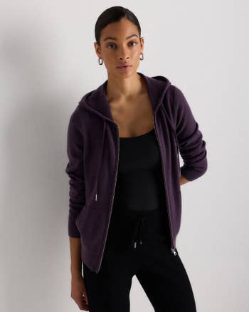 Person in a hoodie and casual outfit poses against a plain background