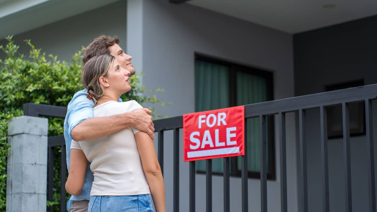 young-couple-with-red-for-sale-sign-on-a-house-fence