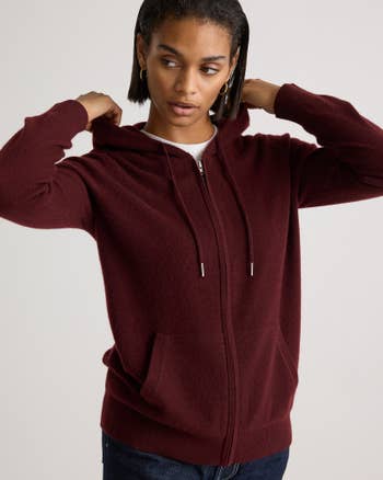 Person wearing a cozy zip-up hoodie with a hood, looking to the side, adjusting the hoodie strings